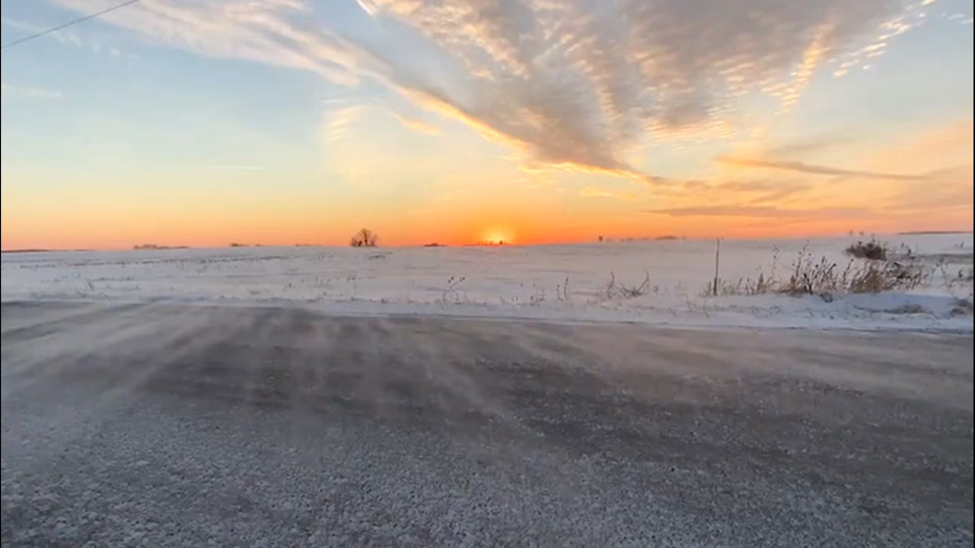 The sun sets above a chilly landscape in Belgium, Wisconsin, on Jan. 20, as strong winds blow snow across the ground.