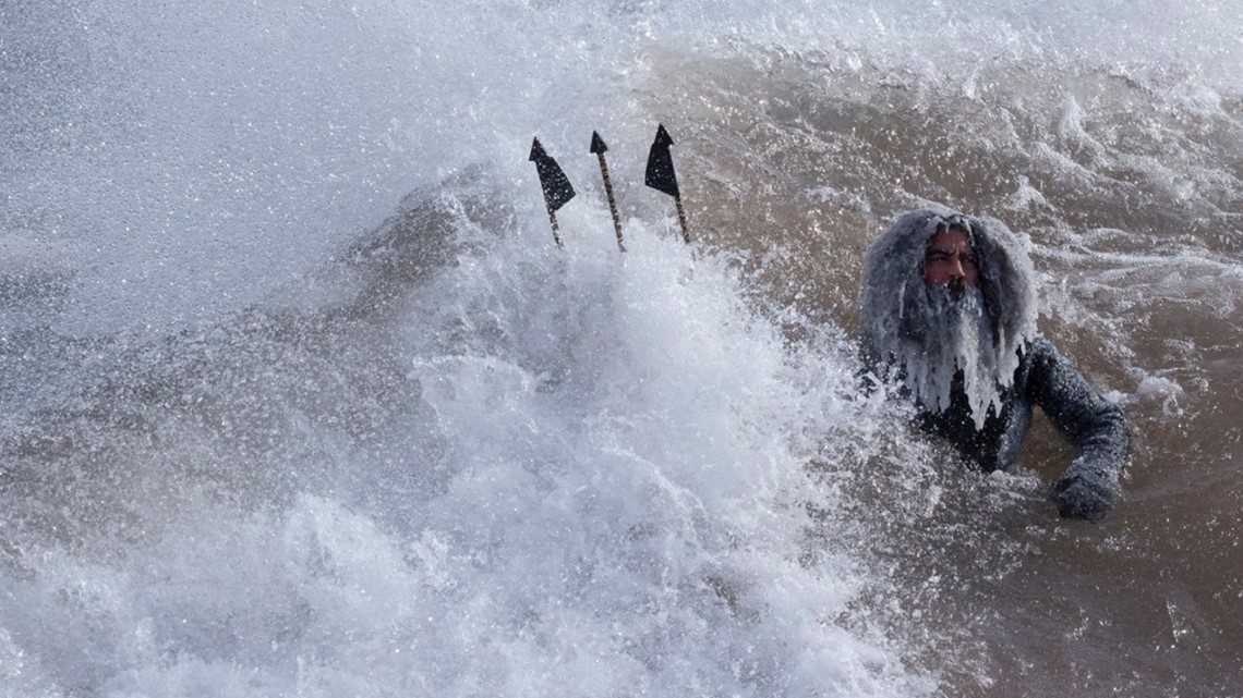 Men holding tridents surf Lake Superior during polar vortex
